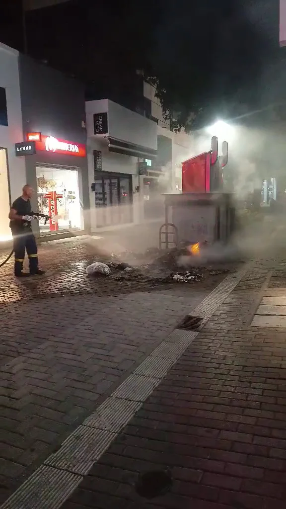 Πυροσβέστης σβήνει τη φωτιά σε κάδο απορριμμάτων.